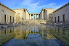 Frontal view of Palais de Tokyo in Paris, with tall columns, sculpted reliefs, and a shallow reflecting pool.