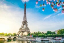Vue sur la Tour Eiffel depuis la Seine par une journée ensoleillée, avec les bateaux amarrés au pied de la Dame de fer, point de départ des croisières promenades, déjeuners et dîners sur la Seine.